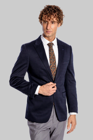 Man wearing a navy blazer, white shirt, and patterned tie on a gray background