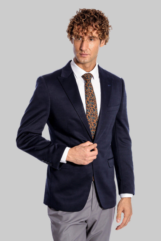 Man wearing a navy blazer, white shirt, and patterned tie on a gray background