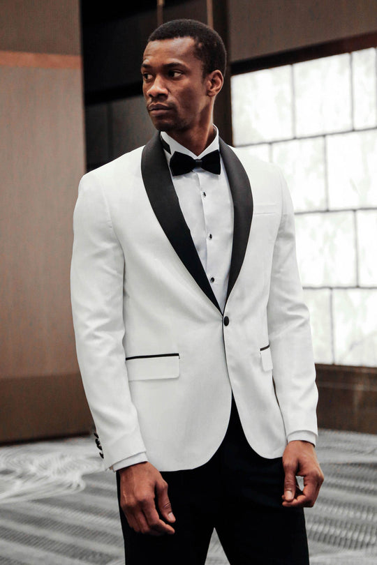 Man wearing a white tuxedo with black lapels and bow tie indoors.