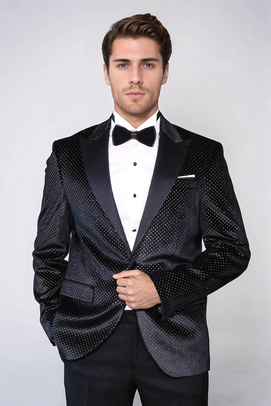 Man wearing a black tuxedo with a white shirt and bow tie on a plain background