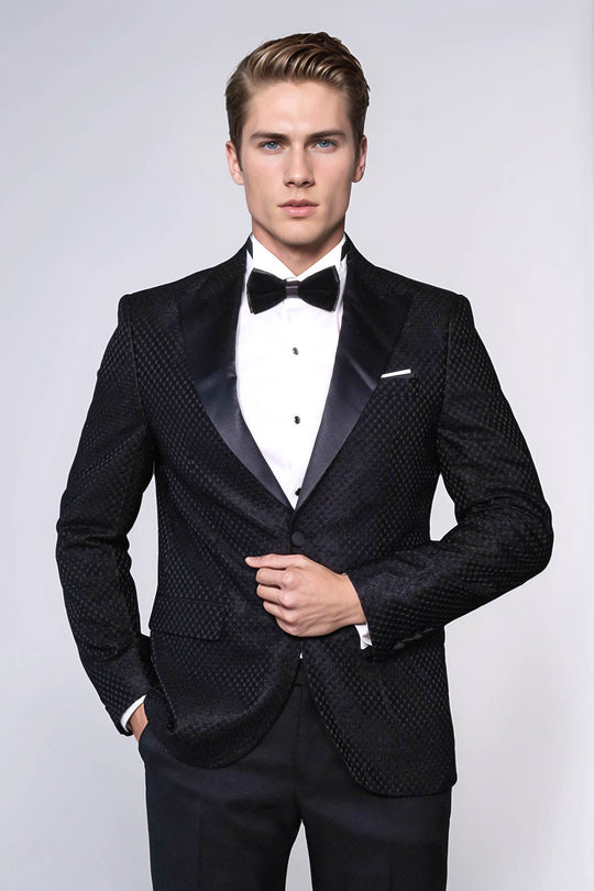 Man wearing a black tuxedo with a white shirt and bow tie on a light gray background