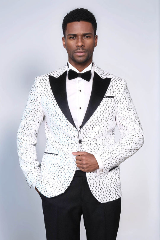 Man wearing a white tuxedo with black polka dots and black bow tie on a light gray background