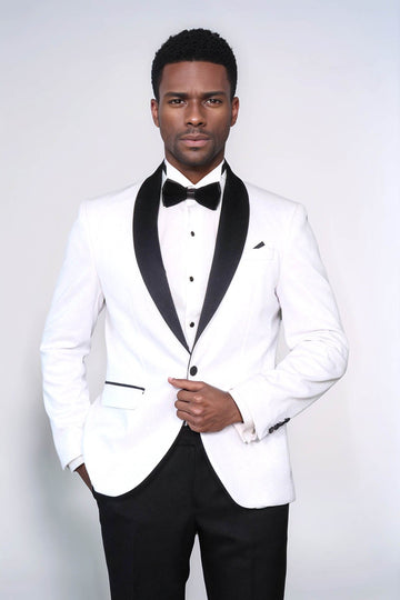 Man wearing a white tuxedo with black lapels and bow tie on a plain background