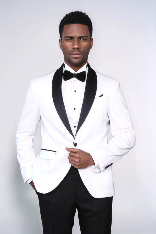 Man wearing a white tuxedo with black lapels and bow tie on a plain background