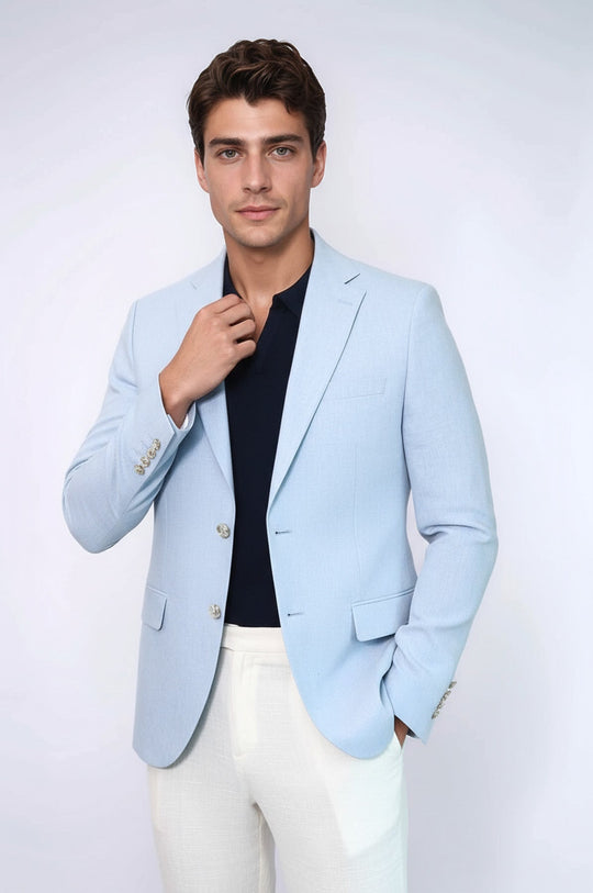 Man wearing a light blue blazer over a black shirt with white pants on a plain background