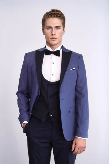 Man wearing a blue tuxedo with a white shirt and black bow tie on a light gray background