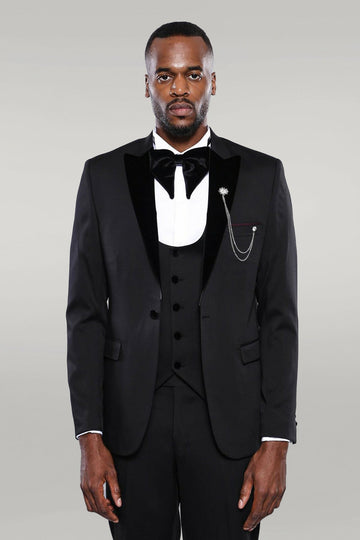 Man wearing a black tuxedo with a white shirt and bow tie on a gray background
