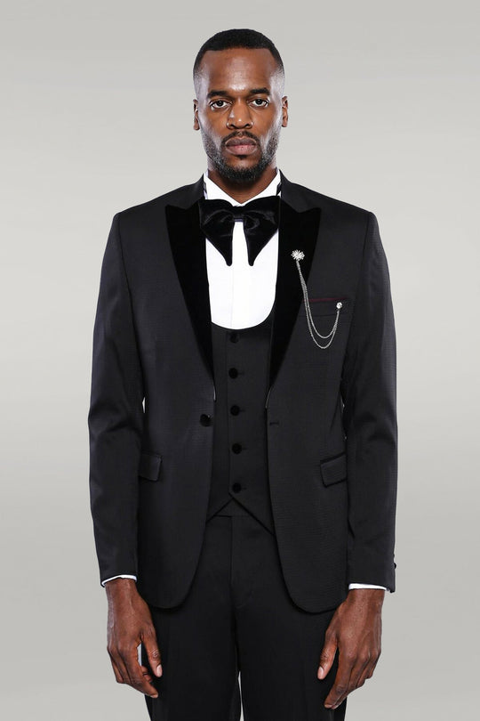 Man wearing a black tuxedo with a white shirt and bow tie on a gray background