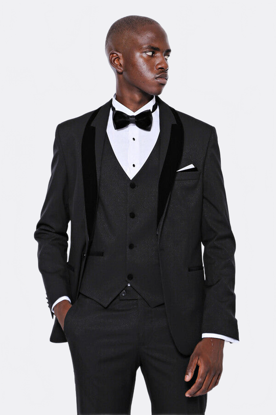 Man wearing a black tuxedo with a white shirt and bow tie on a light gray background